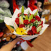 Handheld bouquet of red carnations, yellow gerbera, and white lilies wrapped in white paper