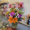 Bouquet of orange lilies, purple flowers, and white daisies in a glass vase