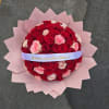 Round bouquet of red and pink roses wrapped in pink paper with a ribbon