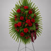 Standing floral wreath of red roses and carnations on an easel with a burgundy ribbon
