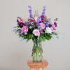 Tall arrangement of pink roses and purple flowers in a clear glass vase