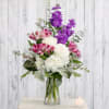 Tall mixed arrangement of white roses and hydrangeas with purple stock and pink alstroemeria in a glass vase