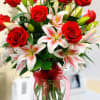 Red roses and white lilies in a clear glass vase with a red ribbon