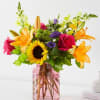 Mixed bouquet with roses, lilies, and a sunflower in a pink glass vase