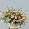 Large mixed floral arrangement in a white vase with pink, peach, and white blooms