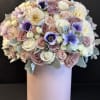 Round bouquet of pastel roses and purple flowers in a pink box