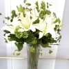 White lilies in a clear glass vase with green filler flowers