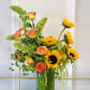 A striking arrangement featuring radiant sunflowers, premium bi-color roses, vibrant Bells of