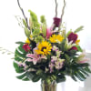 Tall mixed bouquet in a clear glass vase with lilies, roses, and sunflowers