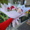 Handheld bouquet of pink and red flowers wrapped in pale pink paper