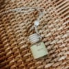 Small perfume bottle hanging from a braided cord on a woven surface