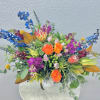 Bright mixed bouquet with orange roses, blue flowers, and pink blooms in a white vase
