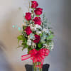 Tall bouquet of red roses in a glass vase with a red ribbon