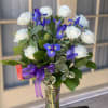 White roses and blue irises in a glass vase with a purple ribbon