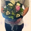 Handheld bouquet of white and pink flowers wrapped in dark paper