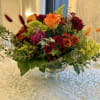 Mixed bouquet in a clear glass vase with orange and burgundy flowers