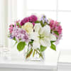 Mixed bouquet of white lilies, cream roses, and pink-purple flowers in a clear glass vase