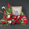 Red roses and white calla lilies arranged around a framed picture.