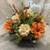 Orange and cream floral arrangement in a low container