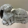 Gray memorial dog figurine beside a stone plaque with engraved text
