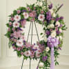 Purple and white floral wreath on a stand with a lavender ribbon