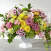 Mixed pink, yellow, and green flower arrangement in a white pedestal vase