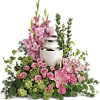 Pink lilies, roses, and carnations arranged around a white cremation urn.
