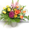 Mixed bouquet of yellow roses, orange tulips, and purple blooms in a vase