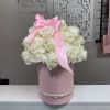 White rose arrangement in a pink hat box with a pink ribbon