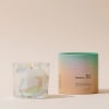 A scented candle in a glass jar beside its pastel cylindrical container