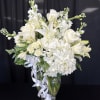 White floral arrangement in a clear glass vase with a white ribbon