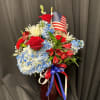 Red, white, and blue floral arrangement in a vase with an American flag