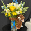 Bouquet of yellow and white flowers in a glass vase with a teddy bear