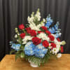 Red roses, blue hydrangeas, and white daisies in a white vase