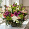 Mixed bouquet of pink, white, and green flowers in a glass bowl vase