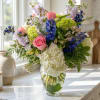 Mixed bouquet of pink roses, white hydrangea, and blue flowers in a glass vase