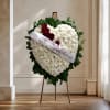 Heart-shaped floral tribute with white flowers, red roses, and a memorial ribbon on an easel