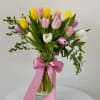 Bouquet of pink, yellow, and white tulips in a glass vase with a pink ribbon