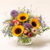 Mixed bouquet with sunflowers, purple blooms, and pink flowers in a glass vase