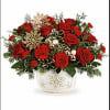 Red roses arranged in a white snowflake vase with holiday accents