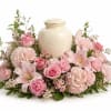 Pink roses and lilies arranged around a cream urn vase