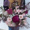 Large bouquet of pink and purple flowers held by a person in an apron