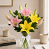 Pink and yellow lilies in a clear glass vase with a white ribbon