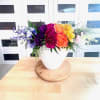 Rainbow floral arrangement in a white vase on a wooden tray
