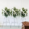 Three white floral standing sprays on easels with ribbon streamers