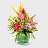 Tropical flower arrangement in a green glass vase with pink and yellow blooms