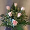 Pink roses arranged in a glass vase with mixed greenery.