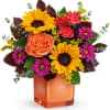 Colorful bouquet of sunflowers, roses, and daisies in an orange glass vase