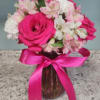 Pink and white flowers arranged in a glass vase with a pink ribbon