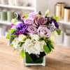 Lavender and white floral arrangement in a clear square vase